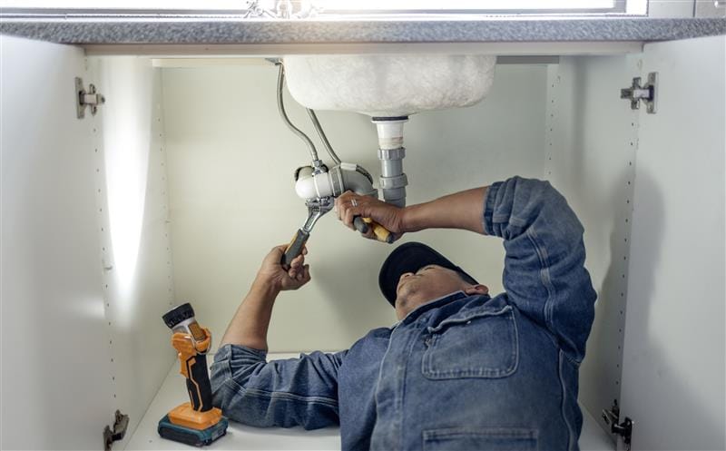 Plumber repairing pipes beneath a bathroom sink in Douglasville