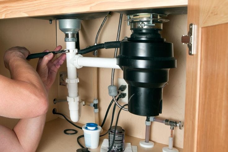 Plumber installing a garbage disposal beneath a kitchen sink in Douglasville