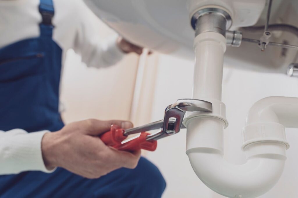 Plumber repairing a white drain pipe beneath a sink in Douglasville